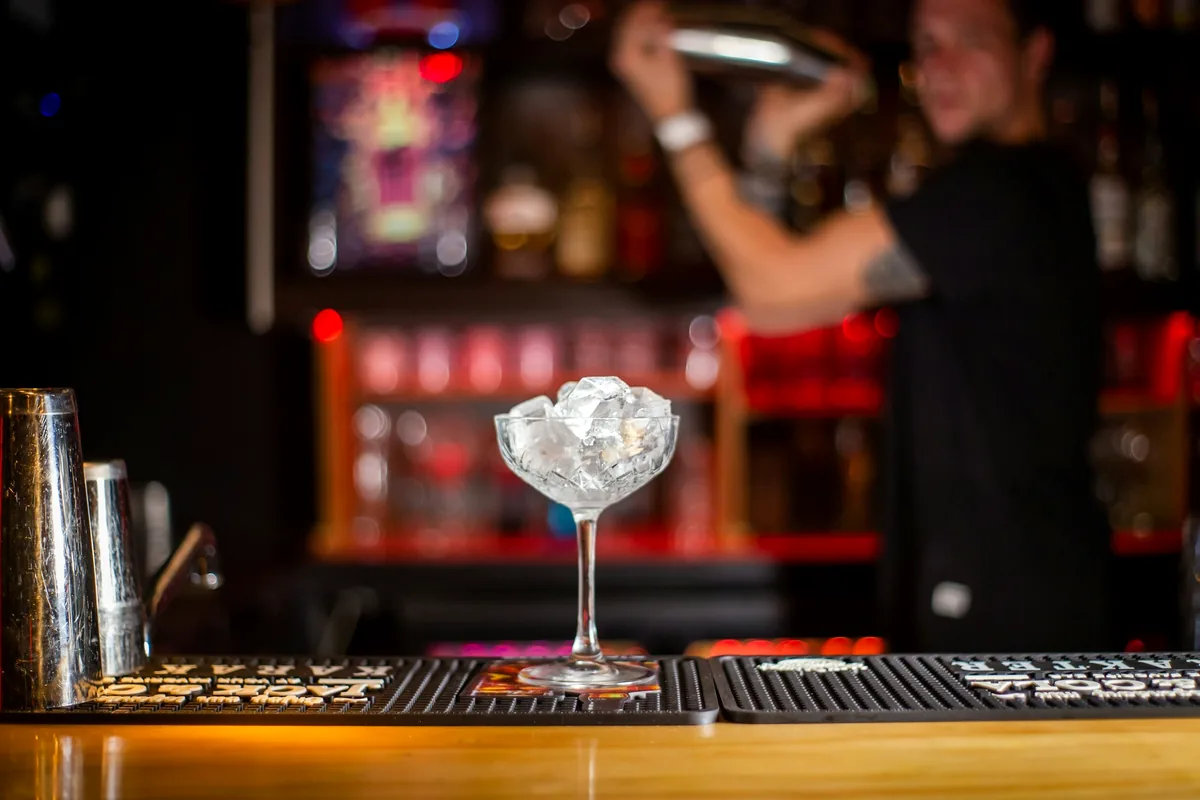 A bartender working in front of a lit back bar lined with bottles