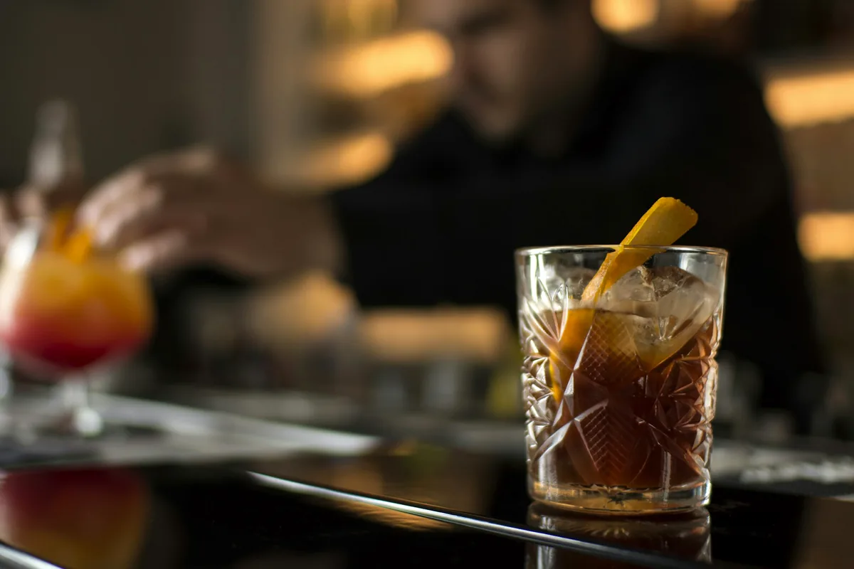 A bartender placing a garnish on an amber drink in a rocks glass