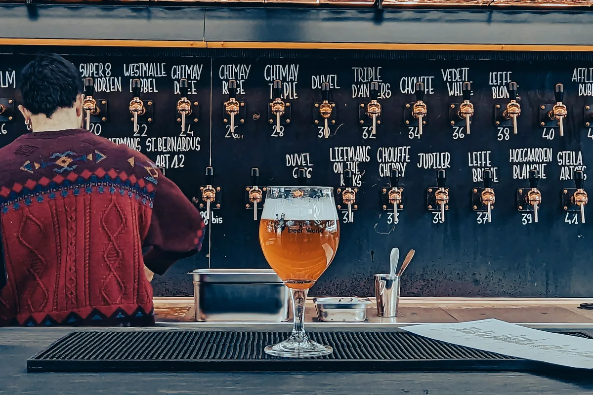 A stemmed glass of Belgian beer on a bar in front of a large chalked beer list