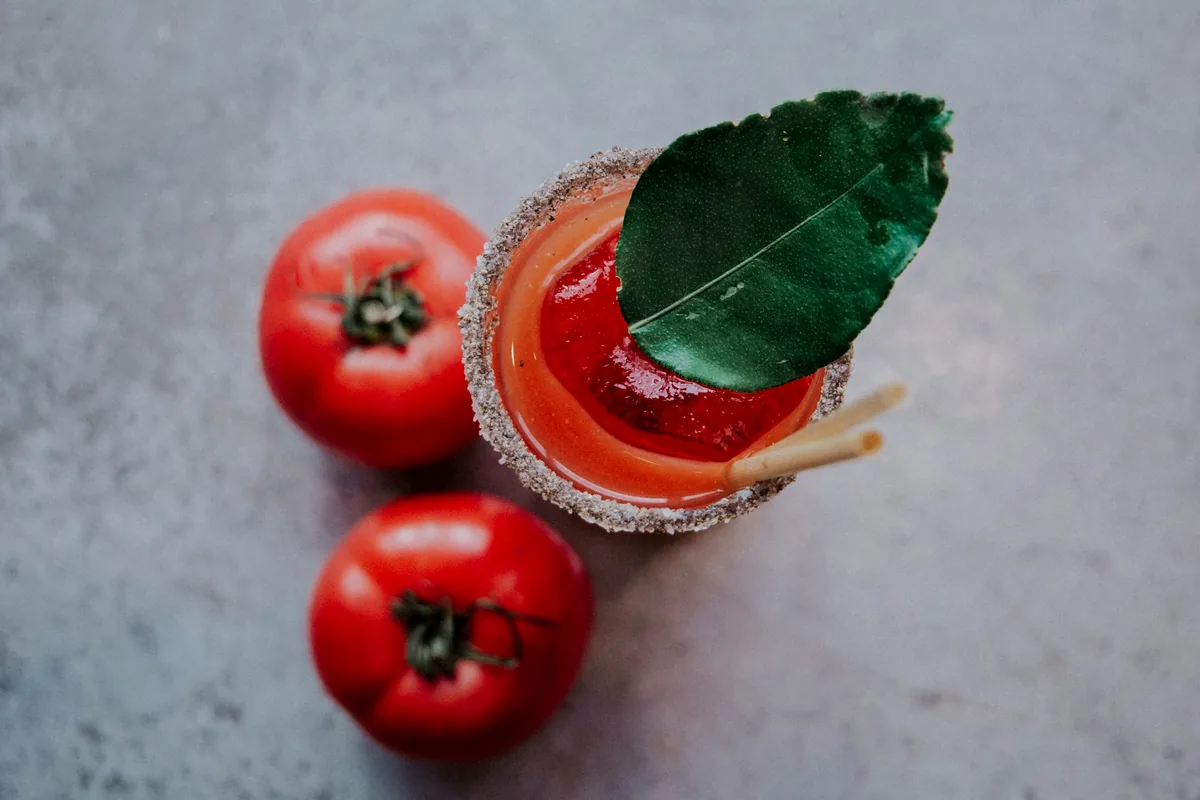 A salt-rimmed tomato cocktail beside two whole tomatoes