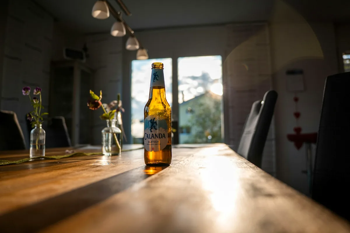 A beer bottle standing on a long wooden table in low sunlight