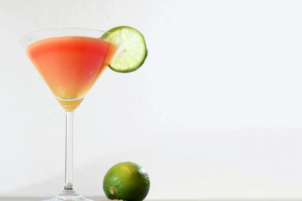 A pink citrus cocktail in a stemmed glass with a lime wheel on the rim