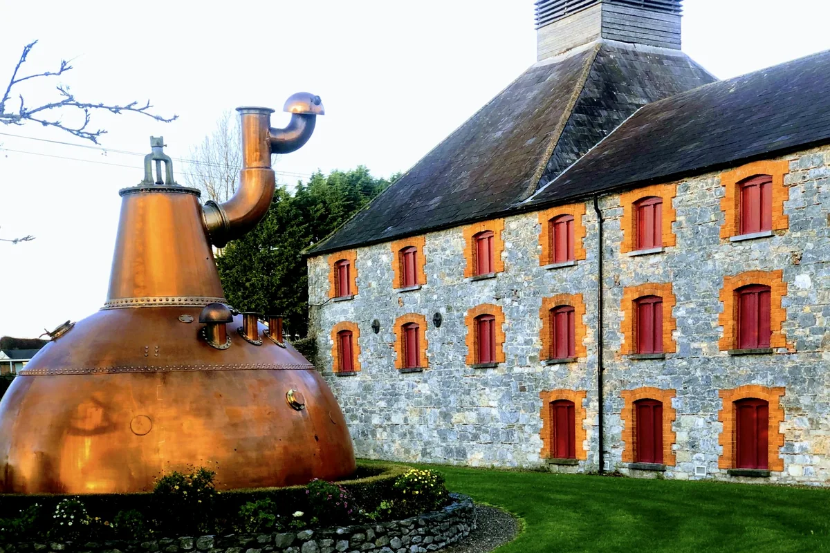 A copper pot still standing outside a stone distillery building