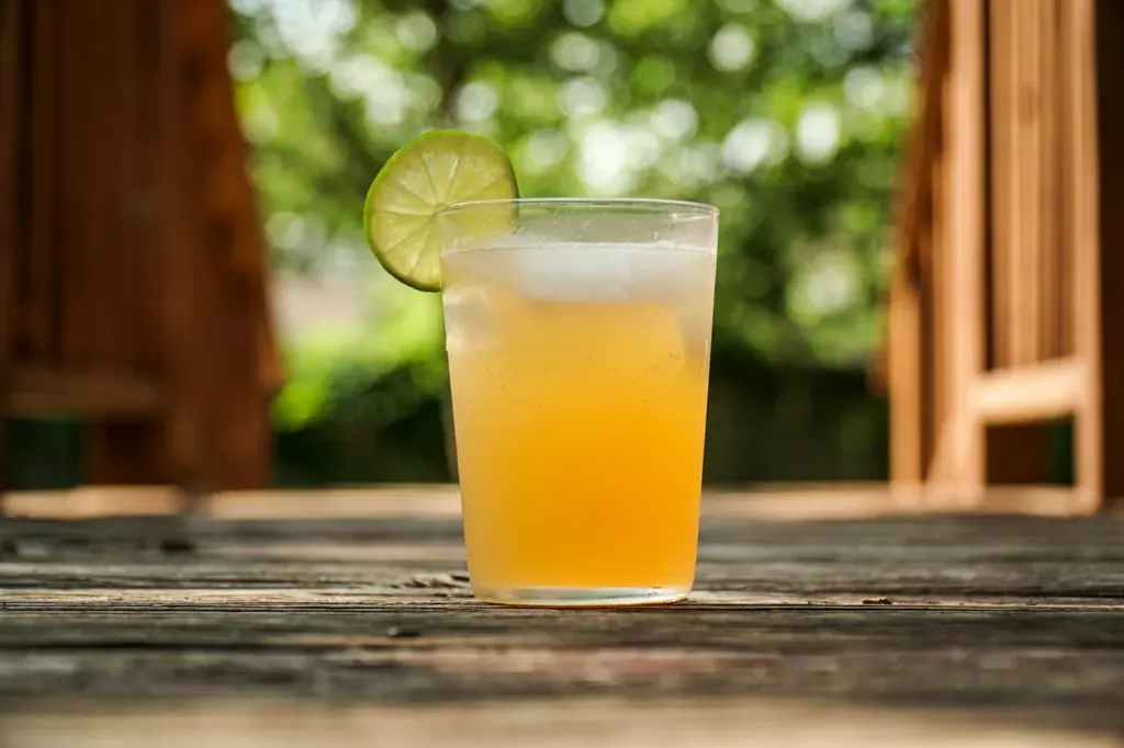 A tall pale rum drink with a wheel of lime on an outdoor wooden table
