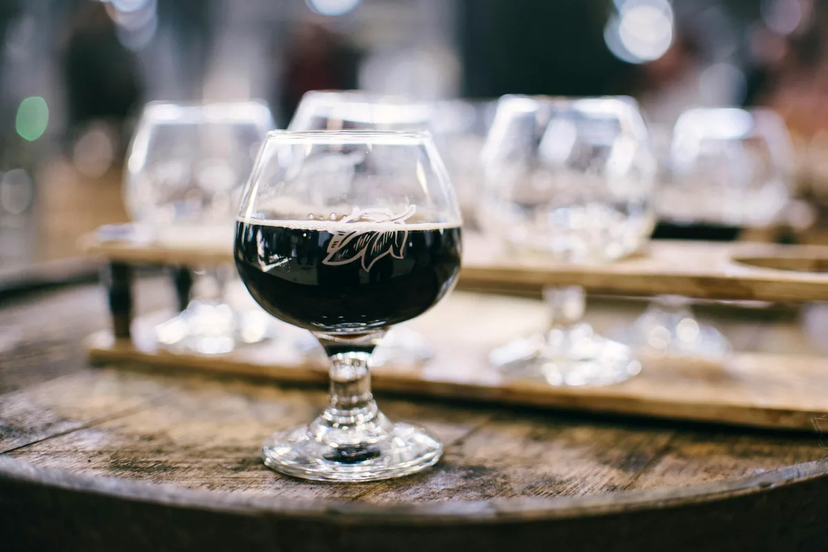 A dark ale in a stemmed chalice on a wooden tasting board