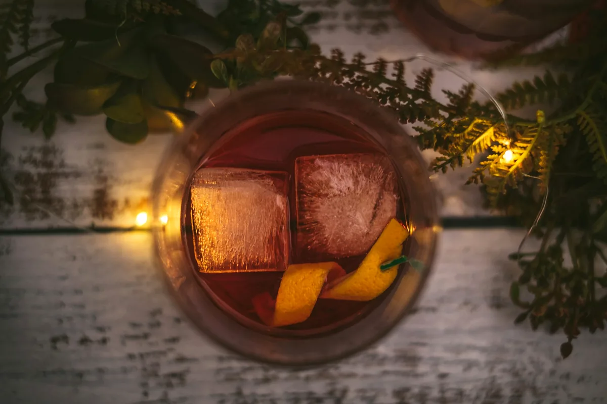 A red stirred cocktail with large ice and an orange twist seen from above