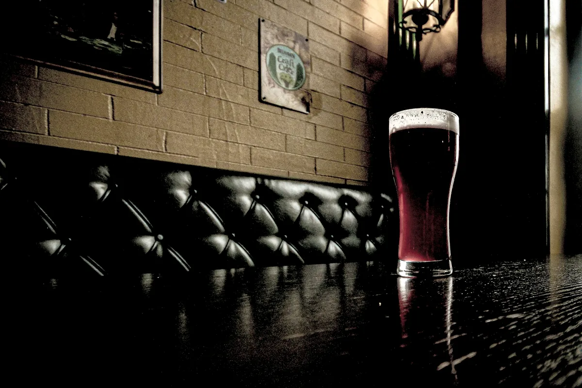 A single glass of dark beer standing on a table in a dim room