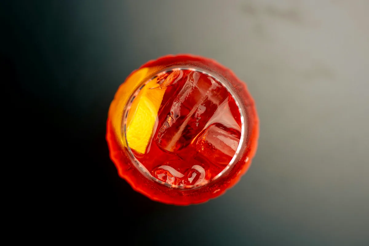 A deep red cocktail over a single large ice cube in a cut glass