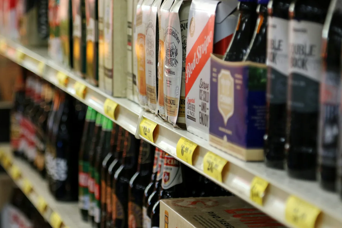 A long shop shelf of beer bottles with printed price tags