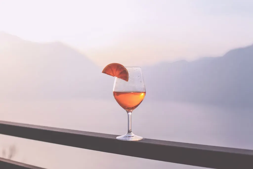 A glass of Aperol Spritz with a slice of orange against a lake and mountains