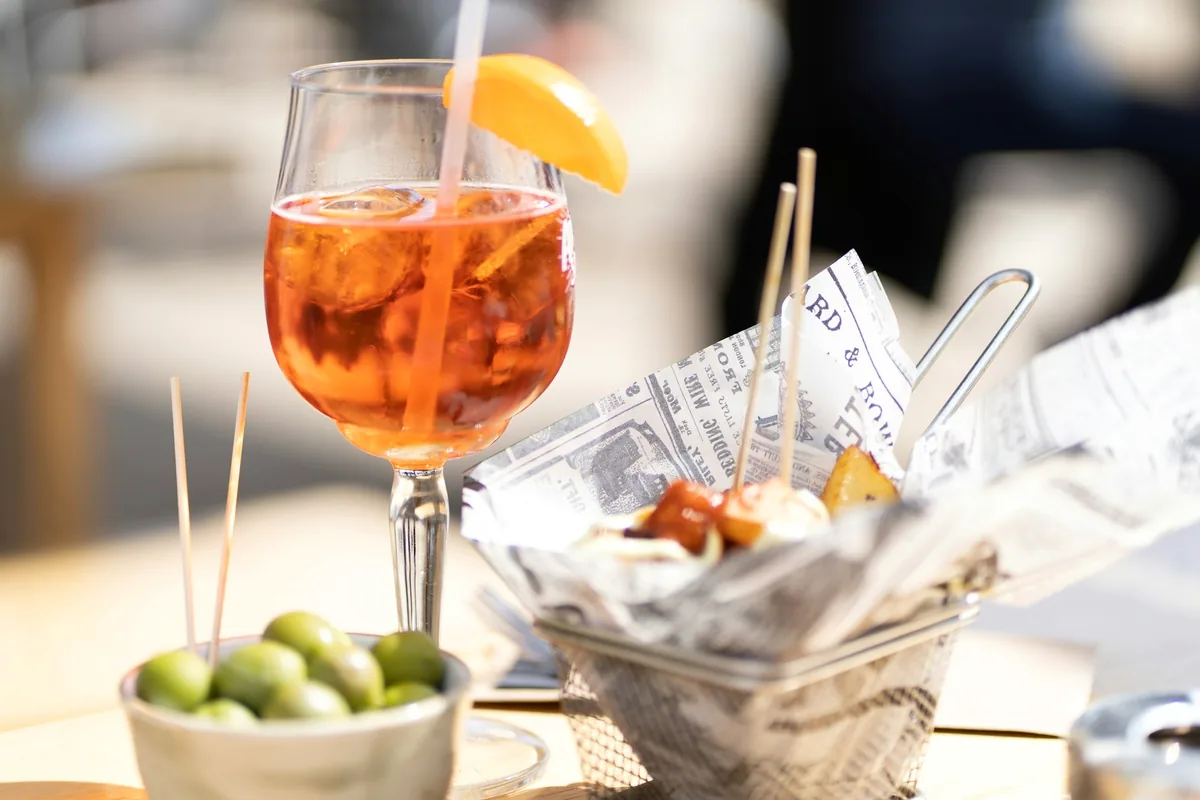 An orange spritz in a wine glass beside a bowl of olives and bar snacks