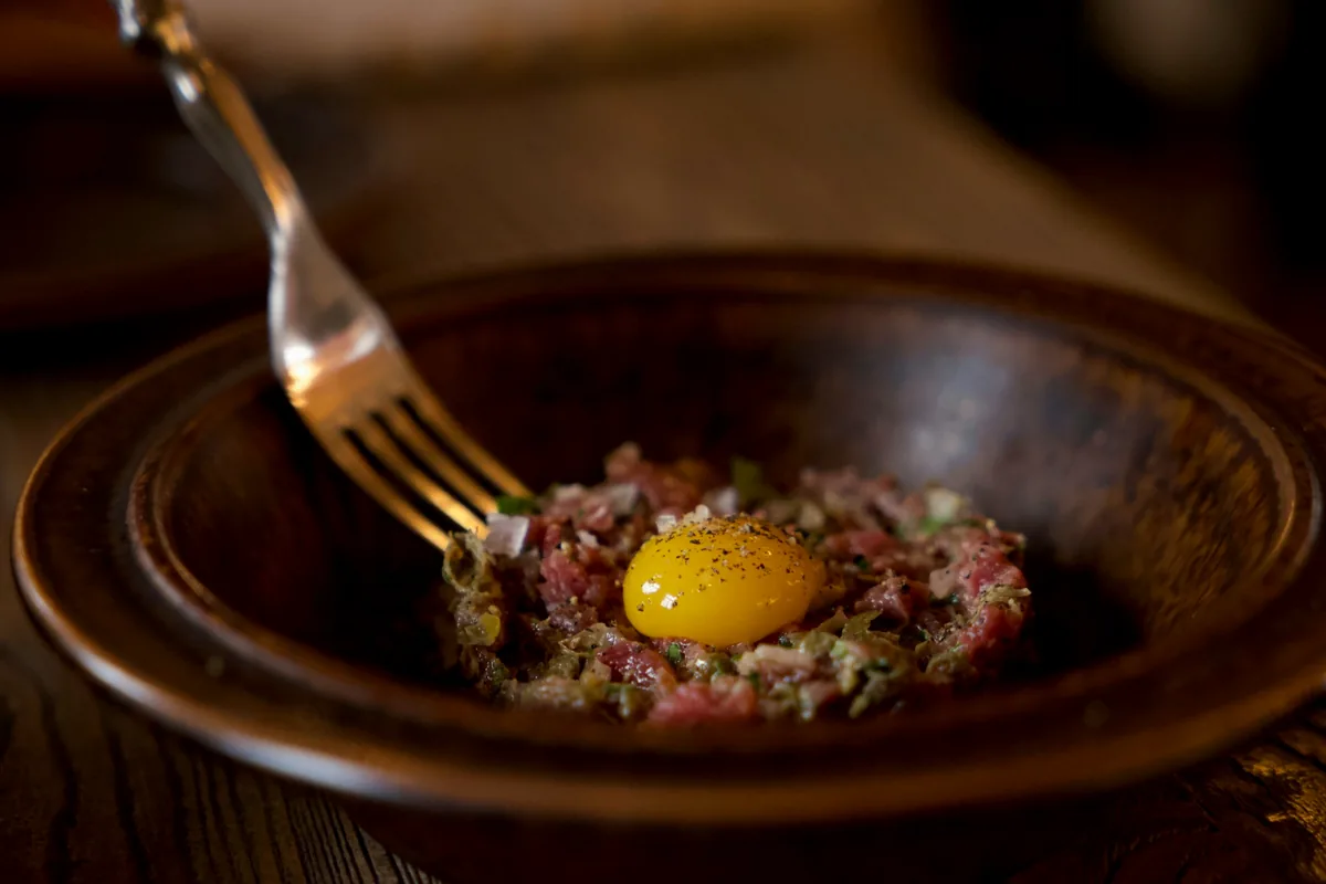 A dark bowl of raw beef tartare with an egg yolk and a fork