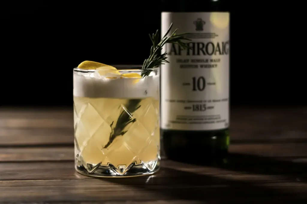A whisky sour in a rocks glass with a thick foam top and a herb garnish