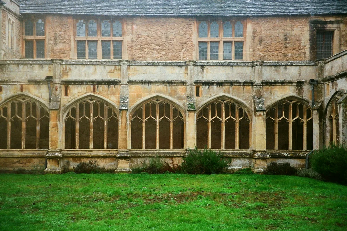 A stone cloister with gothic arched windows around a lawn