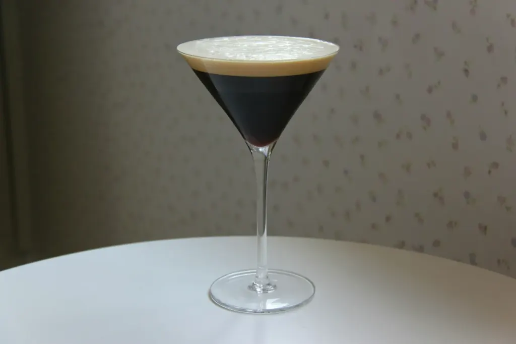 A dark espresso martini in a stemmed glass under a pale crema foam