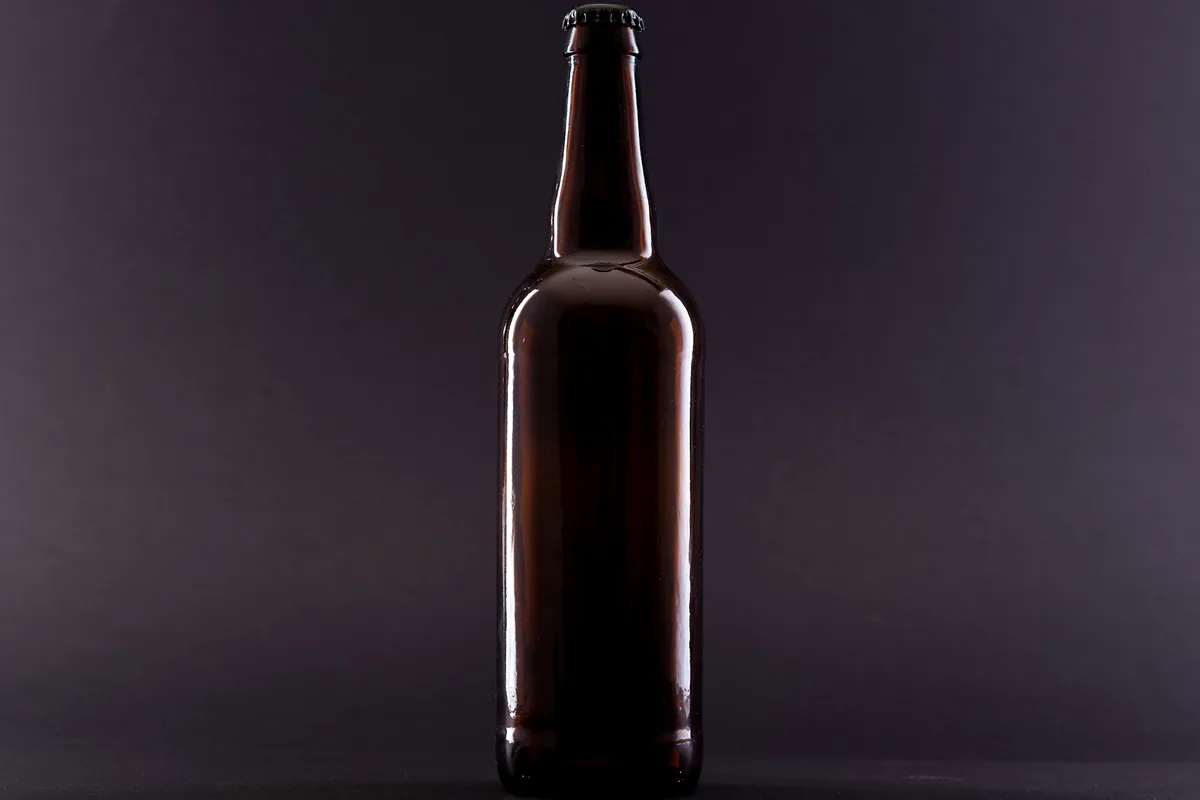 A tall dark beer bottle without a label, lit from one side