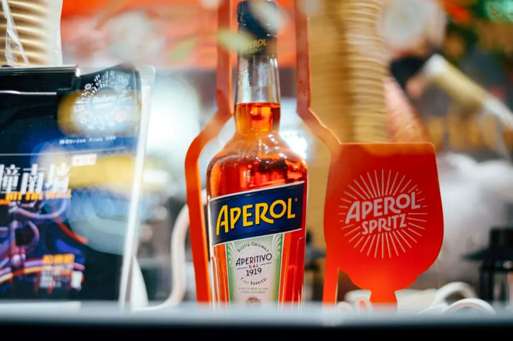 A bottle of Aperol beside a branded Aperol Spritz glass on a bar