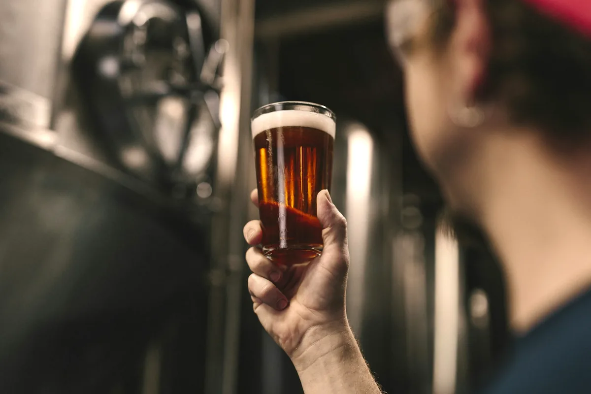 A person holding up a clear glass of beer, shallow focus