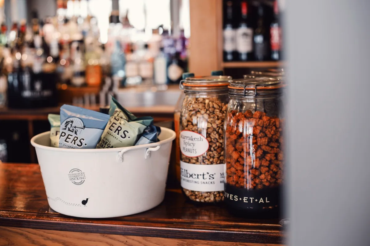 Jars and a ceramic bowl of bar snacks on a counter