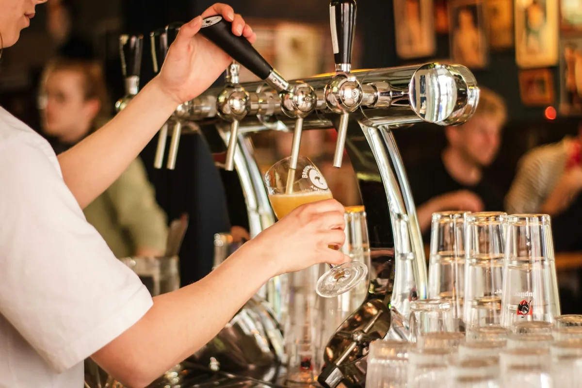 A bartender filling a glass at a bank of taps with clean glassware waiting