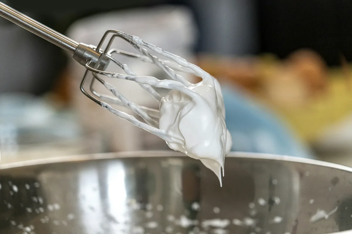 Electric hand-mixer beaters lifted from a bowl of whipped white foam