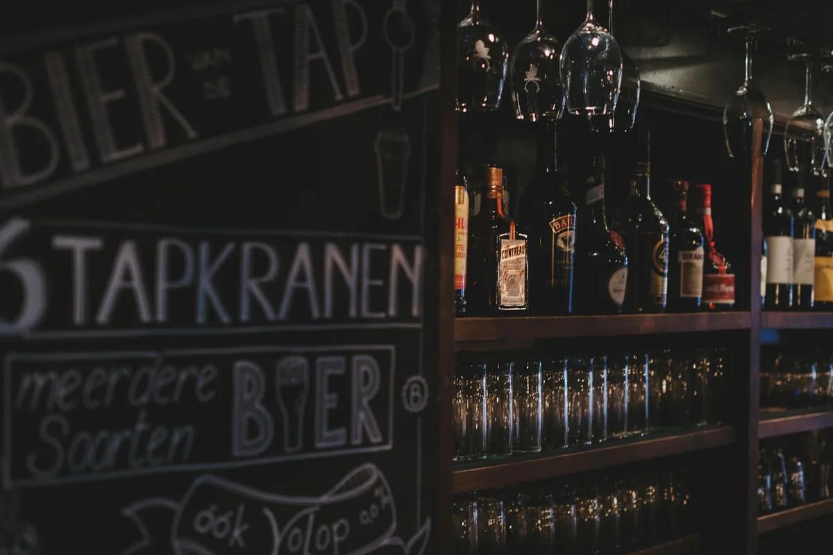A bar interior with a chalkboard listing beer taps and rows of glassware