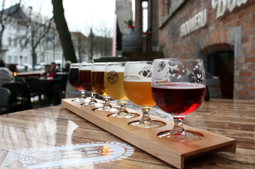 Four small glasses of beer on a wooden paddle outside a brewery
