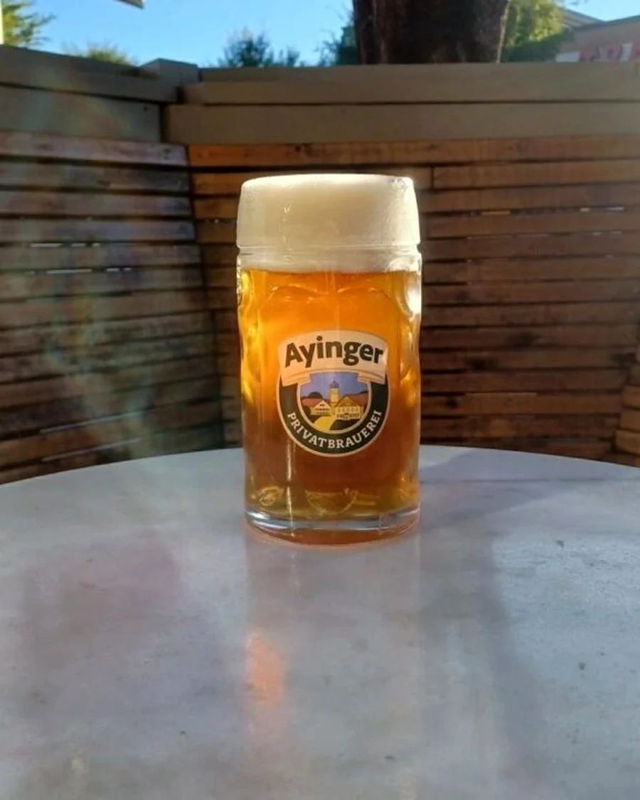 A branded glass mug of pale lager on an outdoor table in full sunlight