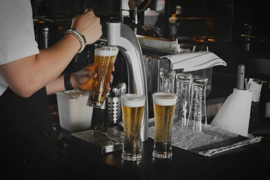 A bartender pouring beer from a tap beside a row of filled tasting glasses