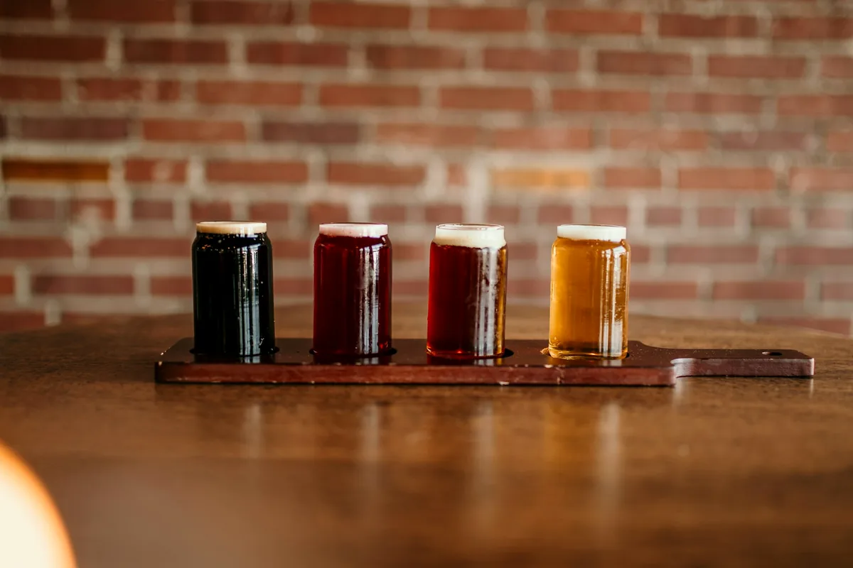 Small glasses of beer in a range of colours lined up on a wooden bar