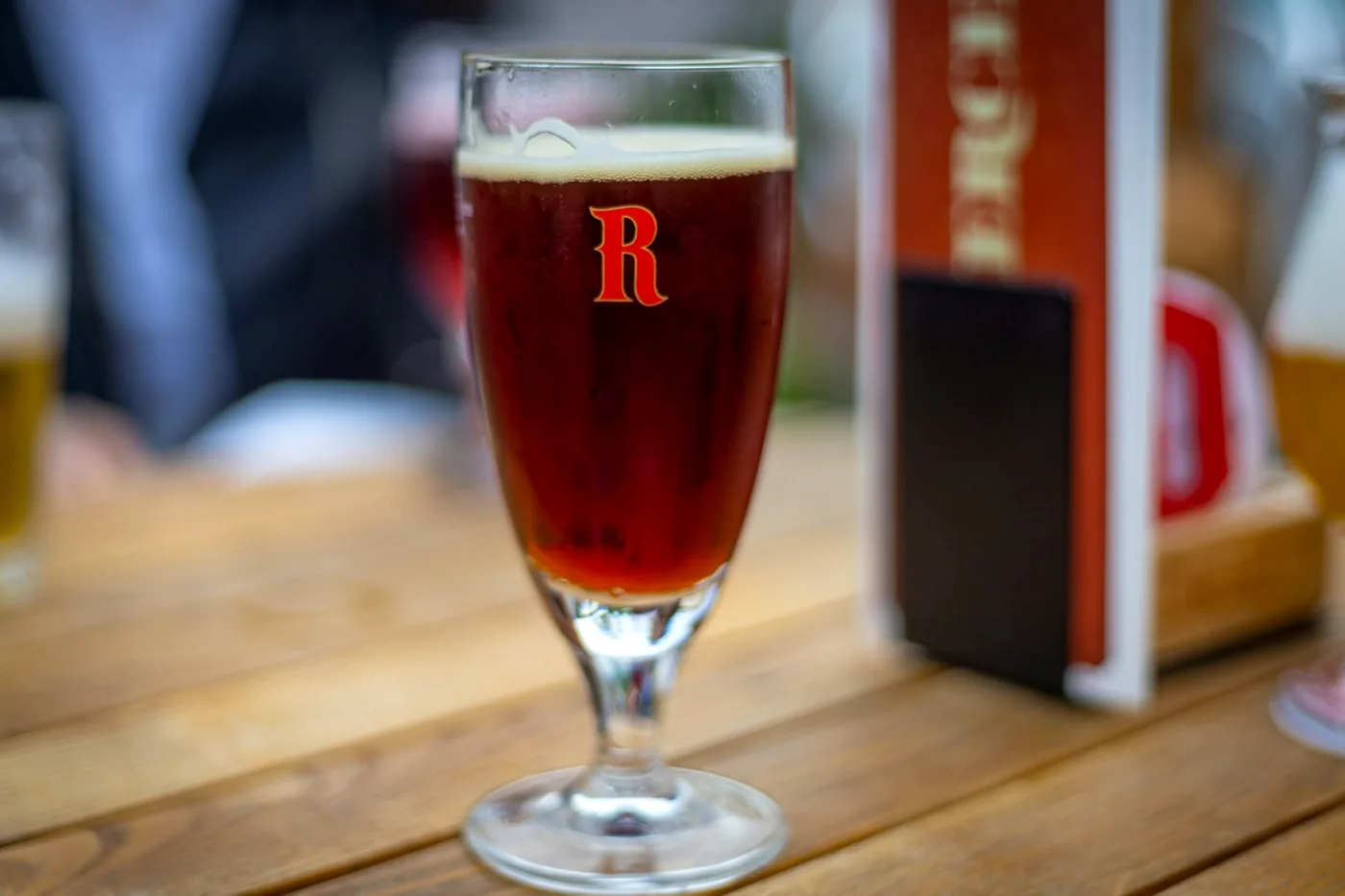 A red-amber Belgian ale in its own branded stemmed glass on a wooden table