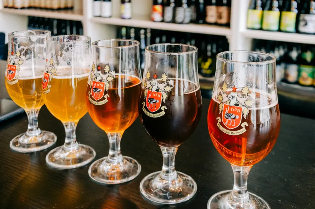 Five Belgian beers in branded glasses running from pale gold to dark brown