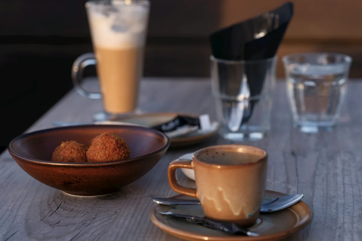 A bowl of bitterballen on a table beside a cup of coffee and a tall glass