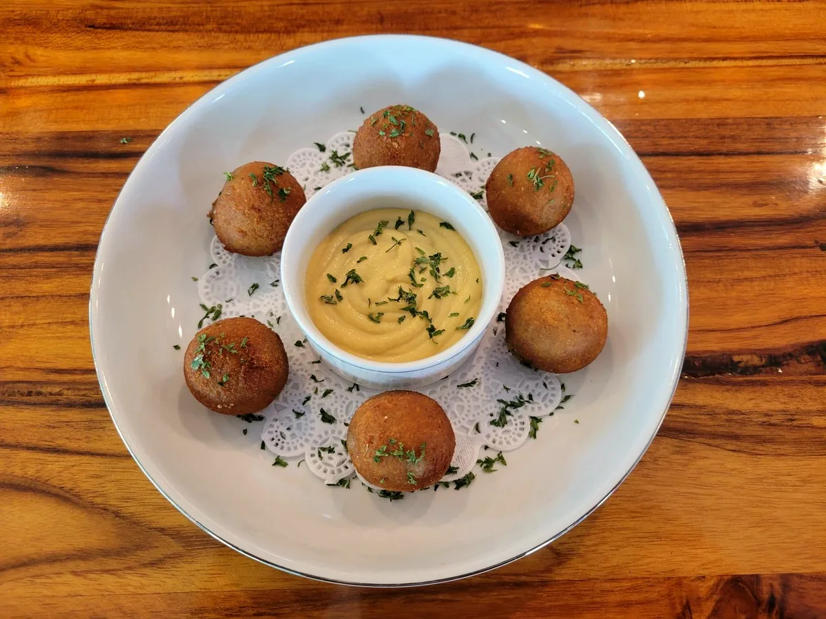 Five bitterballen arranged around a dish of mustard on a white plate