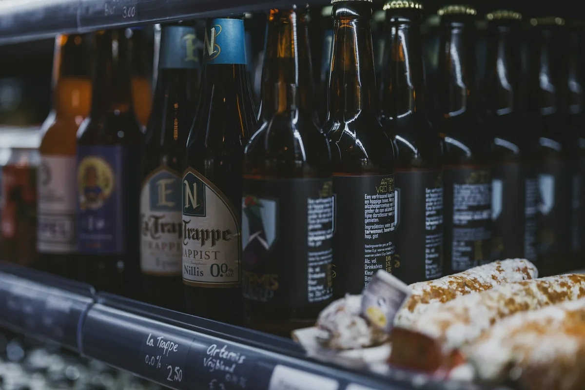 Bottled beers lined up on a shelf behind a bar with a chalked price list