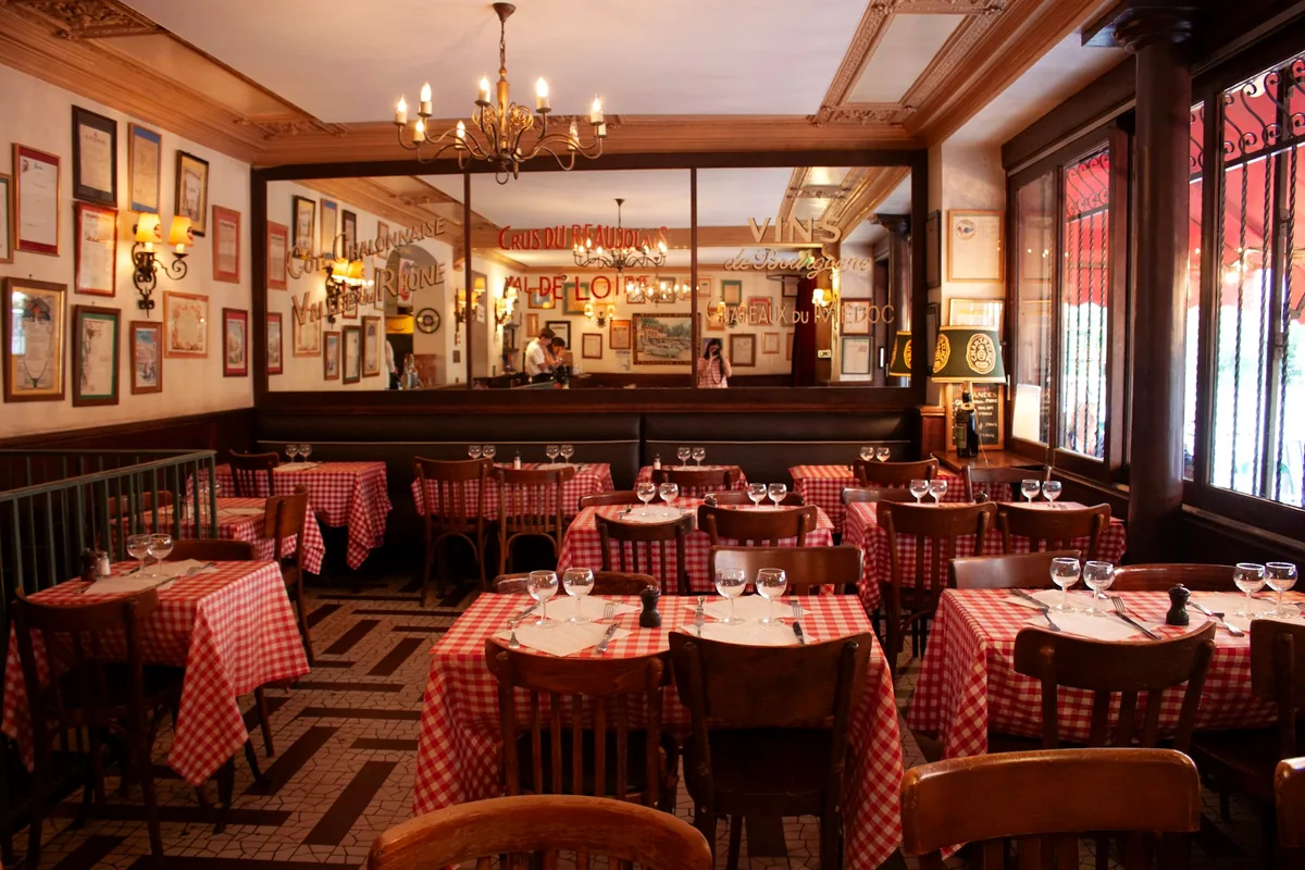 A restaurant dining room with red checked tablecloths and chandeliers