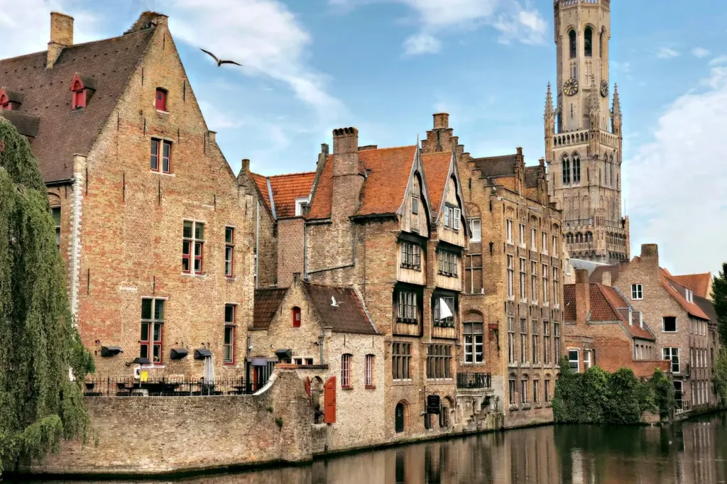 Stepped brick gables along a canal in Bruges with the belfry behind