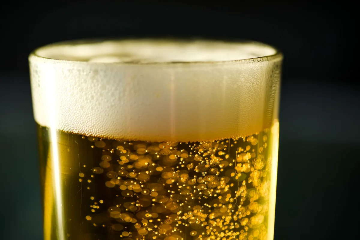 Close-up of carbon dioxide bubbles rising in a glass of pale beer