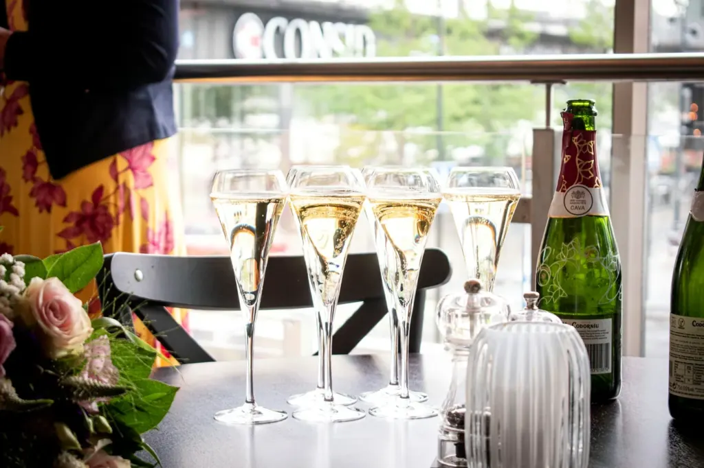 A row of filled sparkling wine flutes on a table beside two bottles