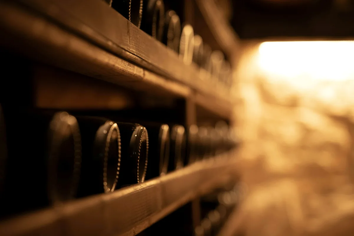 A dim cellar rack of bottles receding towards a warm light