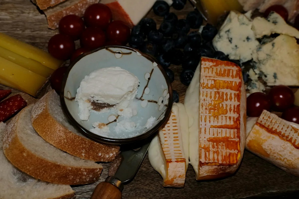 A board of cheeses with bread, grapes and dried fruit