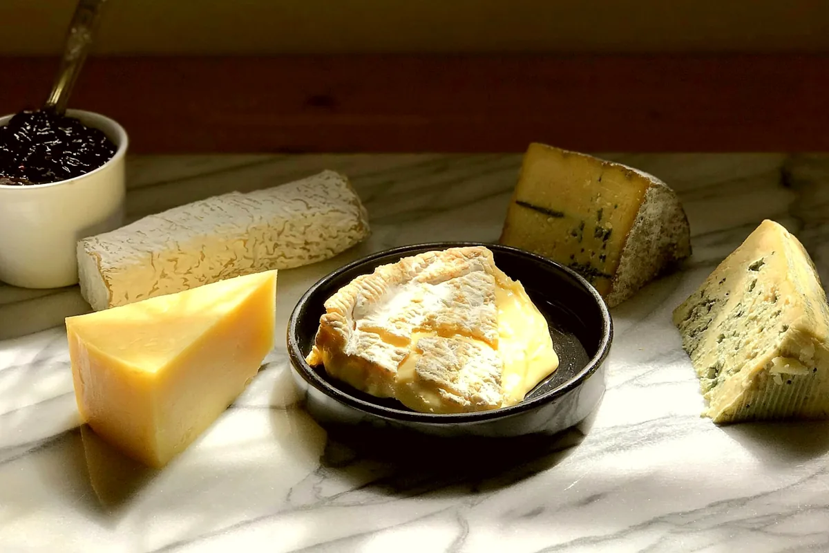 An assortment of cheeses beside a small bowl of jam