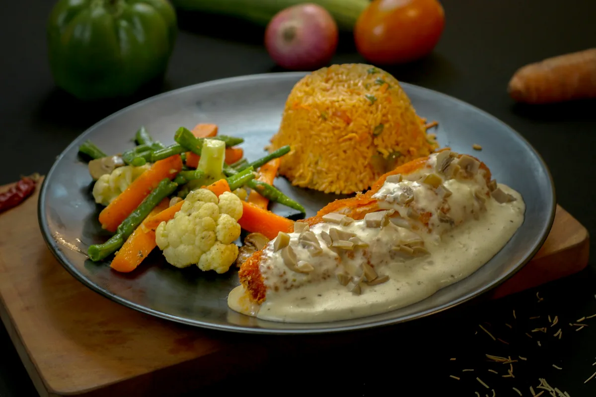A plate of chicken in cream sauce with rice and vegetables