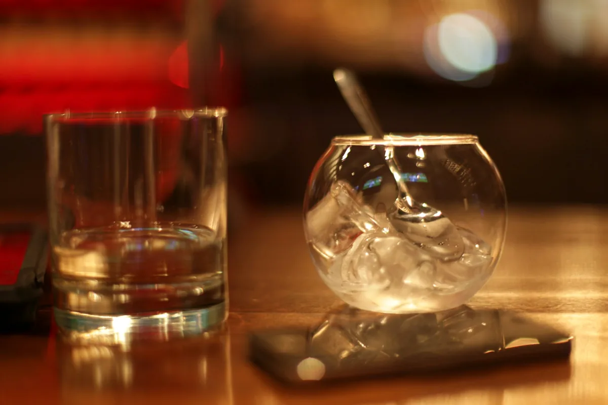 A tumbler of spirit beside a stemmed glass packed with clear ice