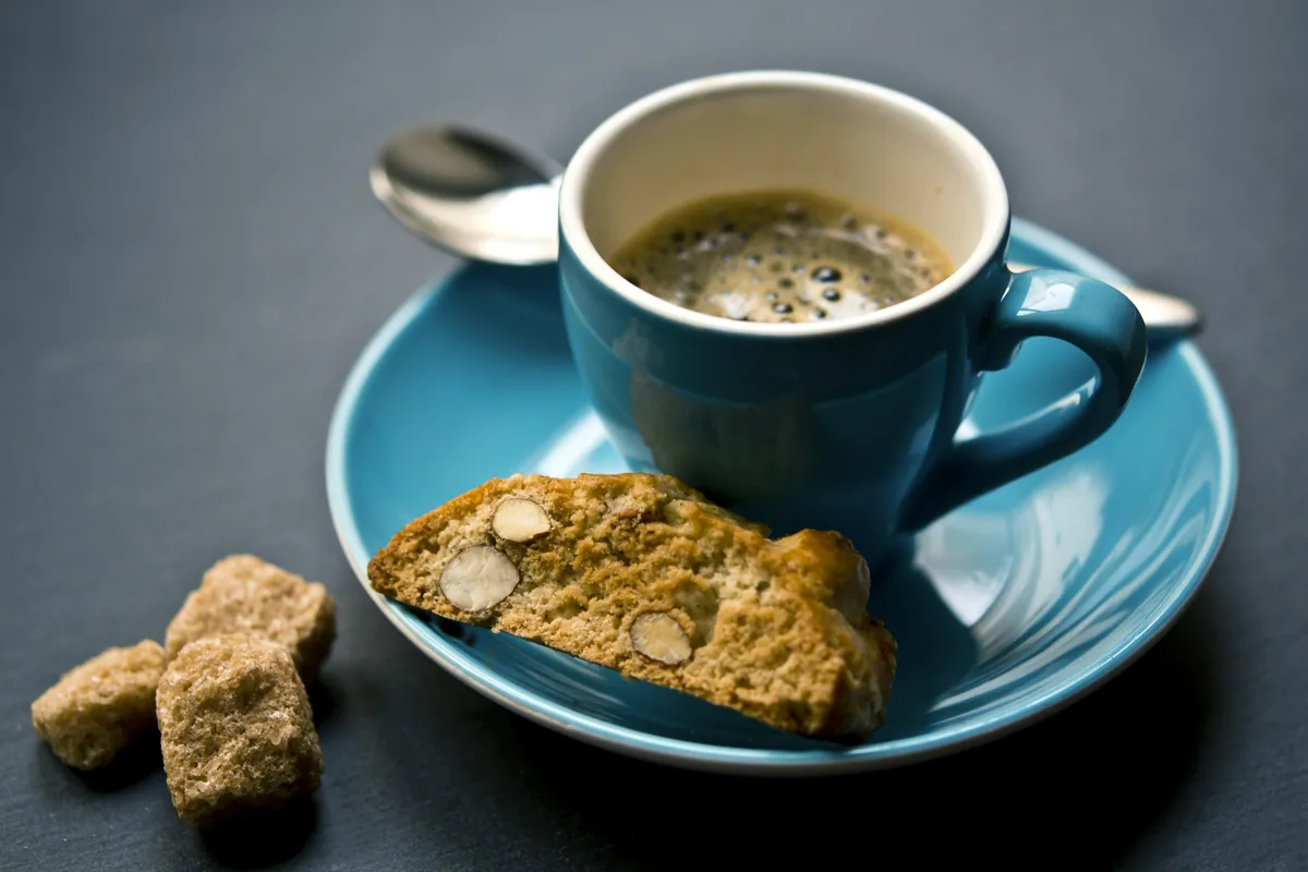 A cup of coffee on a saucer with a biscuit alongside