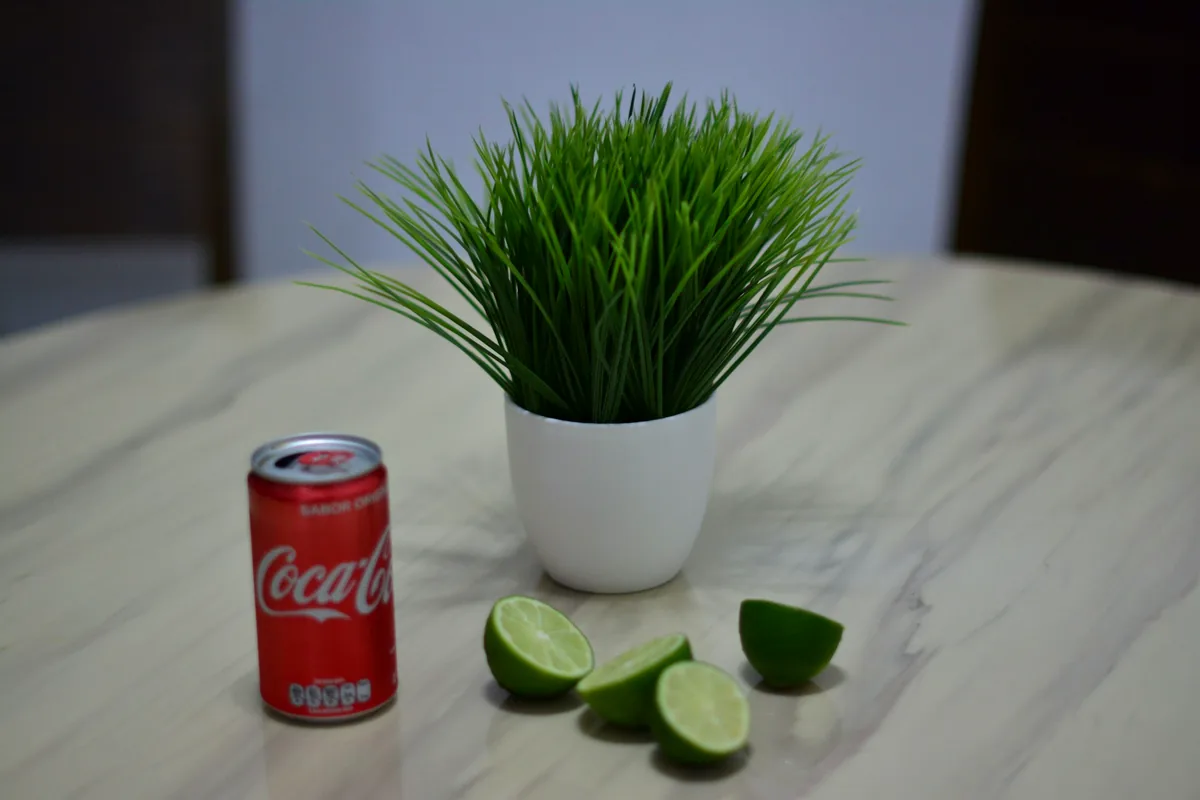 A chilled cola can beside halved and quartered limes on a marble surface
