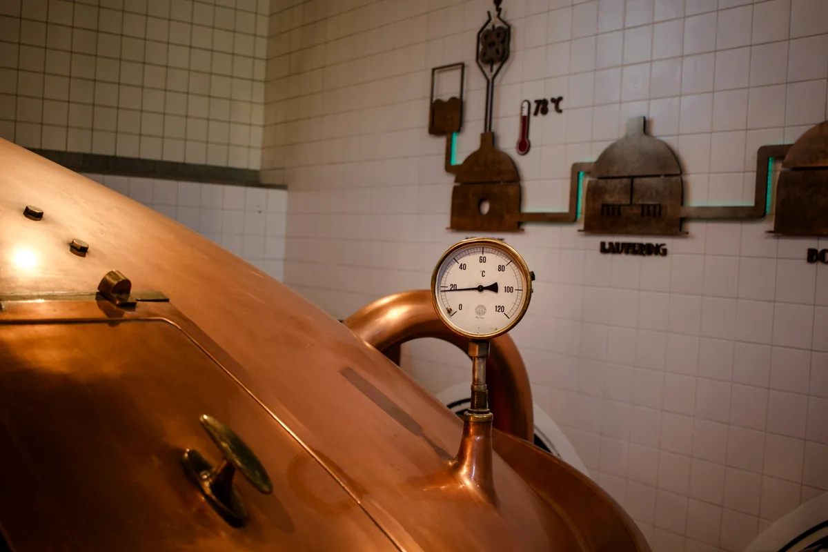 A copper brewing vessel with a pressure gauge in a tiled brewhouse