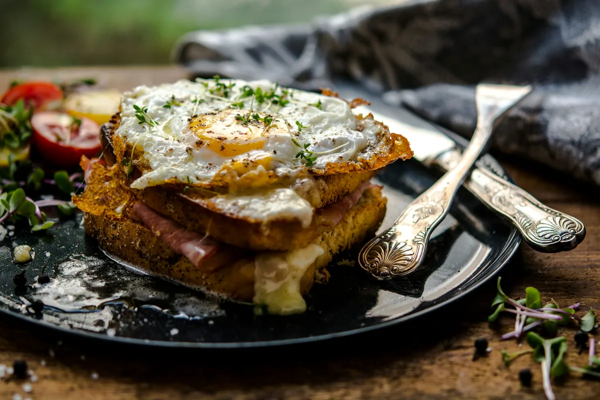 A toasted ham and cheese sandwich topped with a fried egg on a dark plate