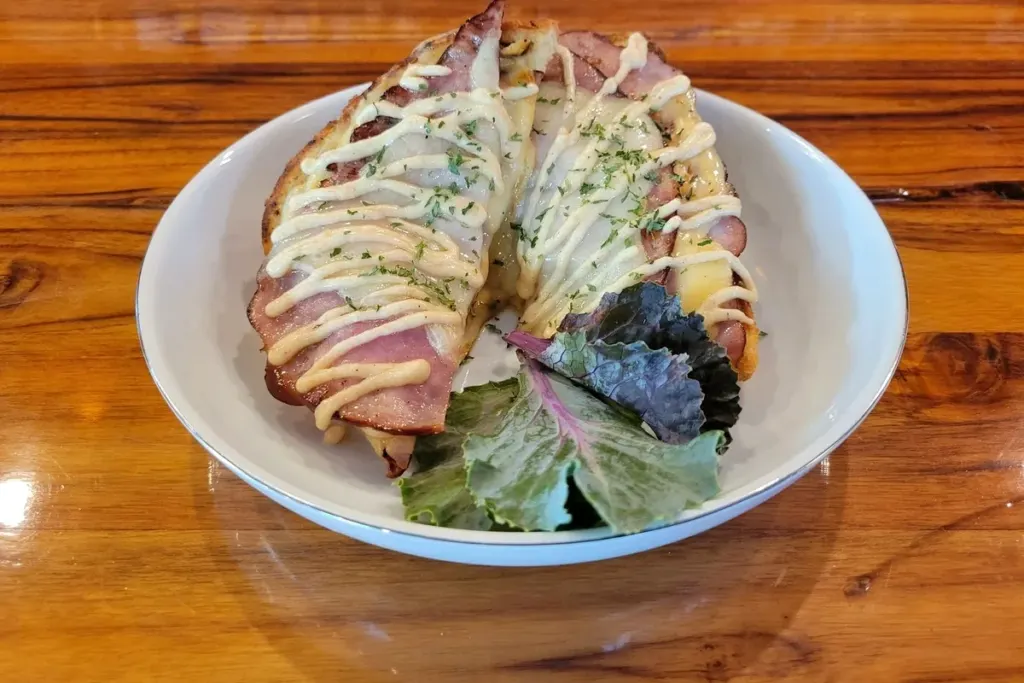 A grilled ham and cheese sandwich topped with beer cheese sauce, served with frites
