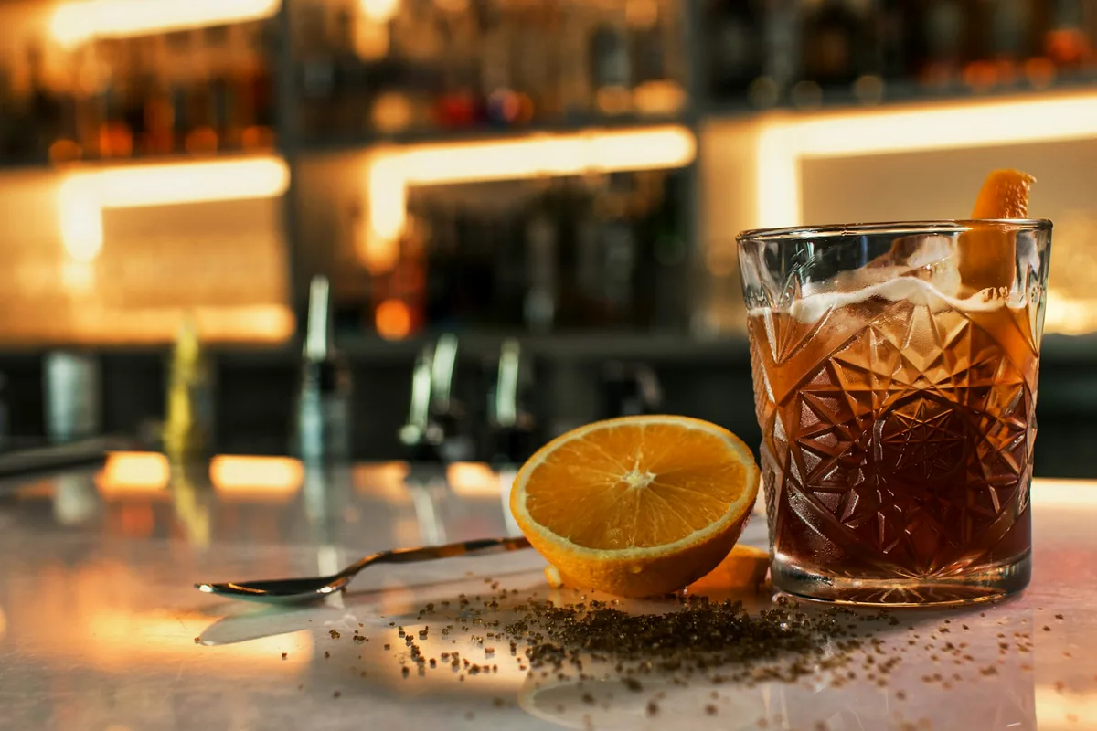 An amber drink in a cut-glass tumbler with orange on a warmly lit bar